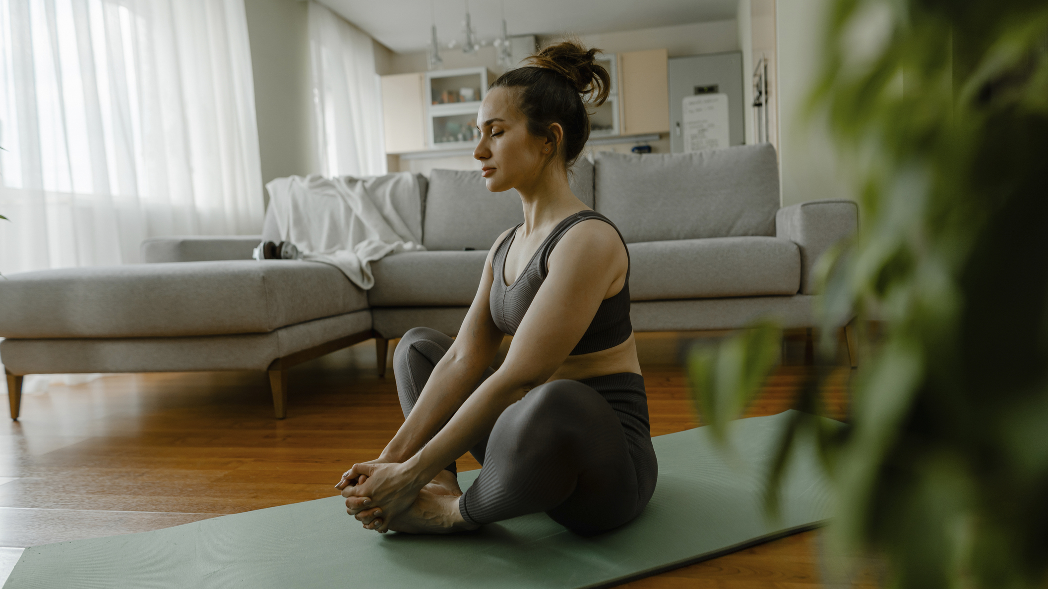 Woman sits on a yoga mat in seated butterfly pose in a domestic setting