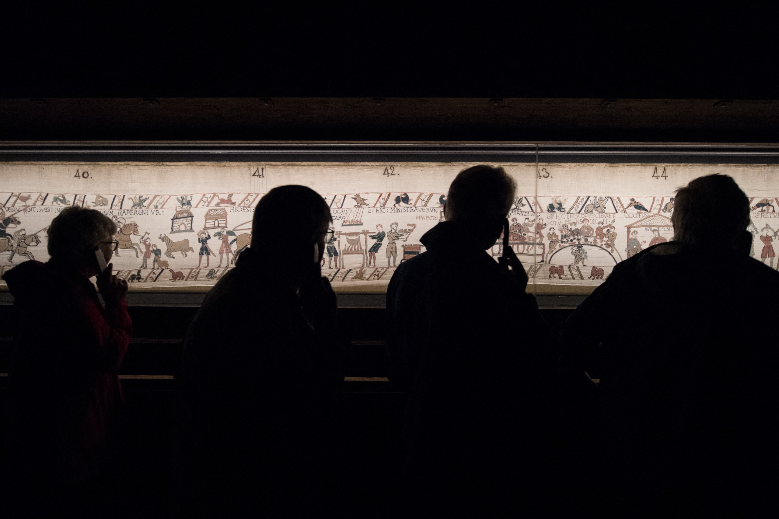 People silhouetted looking at the Bayeux Tapestry