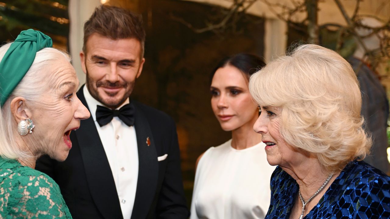 Queen Camilla in a blue evening gown talking to Helen Mirren, wearing a green headband and dress, with Victoria and David Beckham looking on 