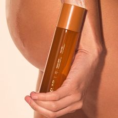 stylized image of hand holding cyklar vanilla vitamin c body oil against wet skin