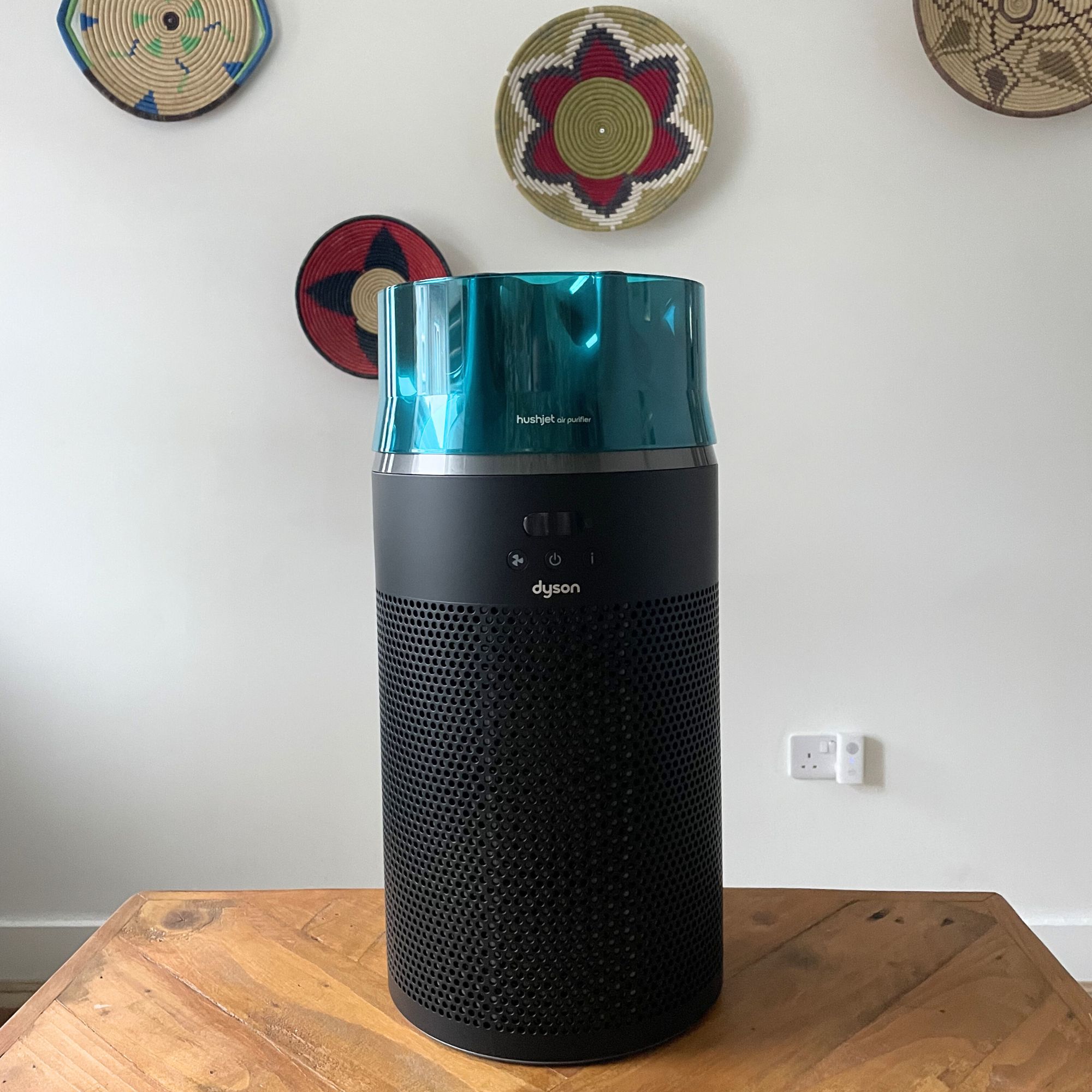 Black and teal Dyson Hushjet Air Purifier sitting on a wooden table in front of a white painted wall