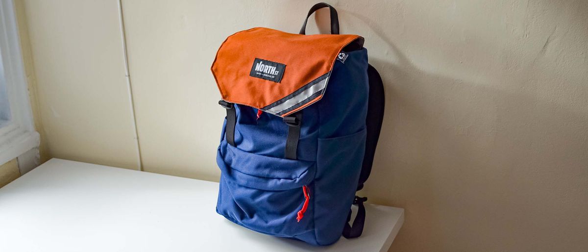 A North St. Belmont in Navy with an Orange flap sitting on a desk