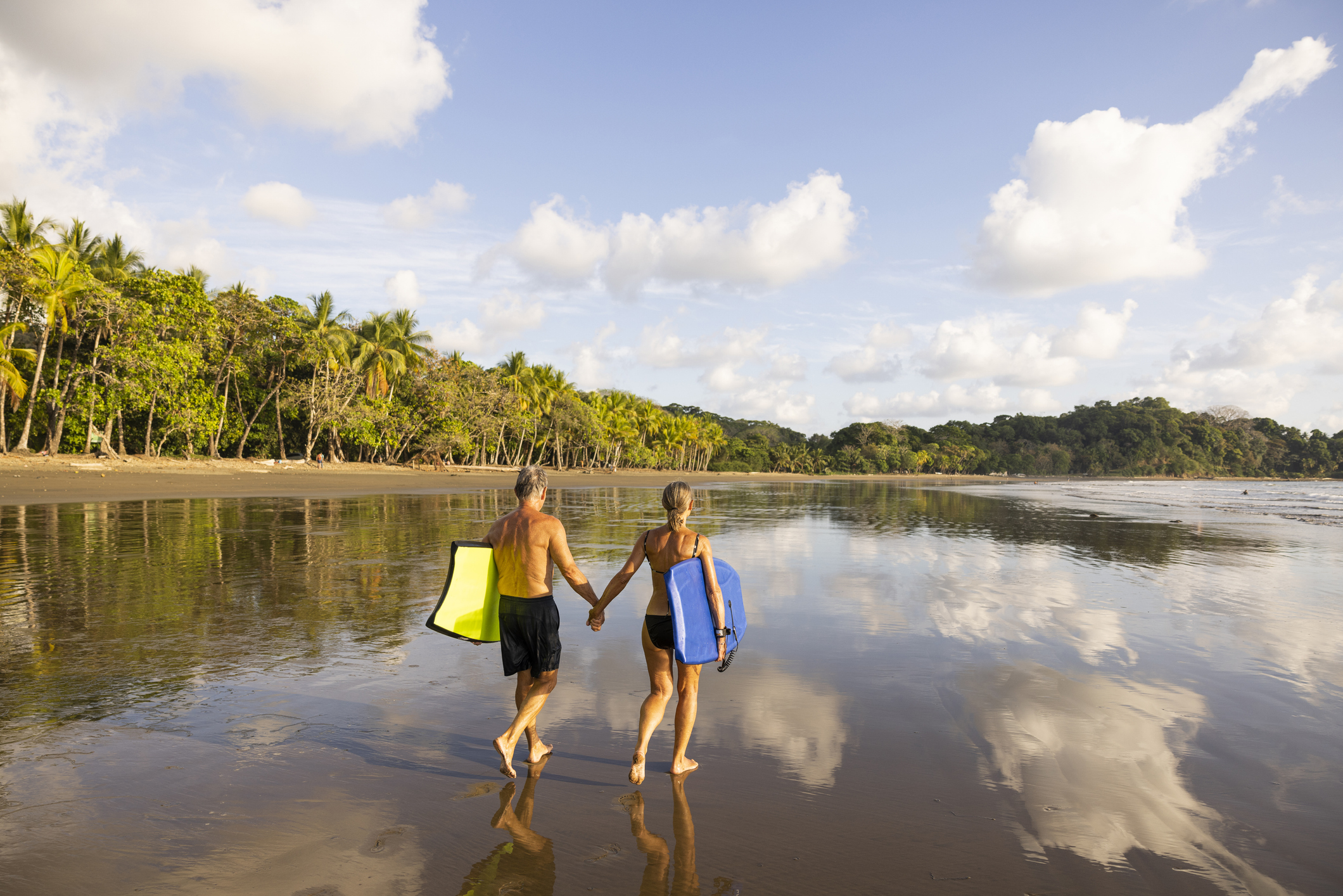 A senior couple holding boogy boards ready for a fun day in the ocean.