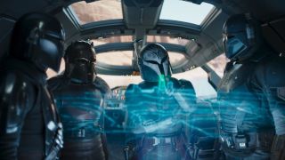 characters in silver armor stare at a blue hologram display inside a spaceship
