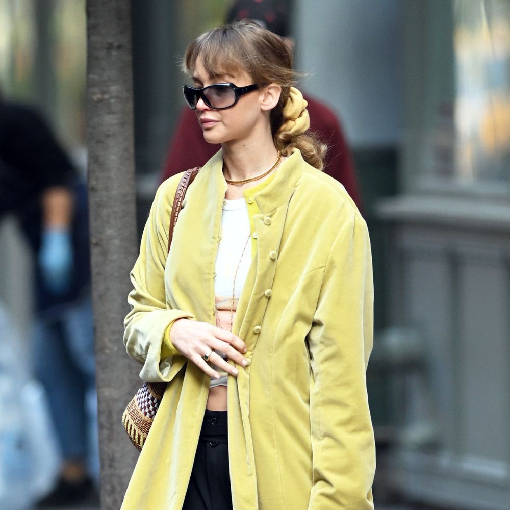 Jennifer Lawrence walks down the street wearing a house coat with a white t-shirt and black trousers.