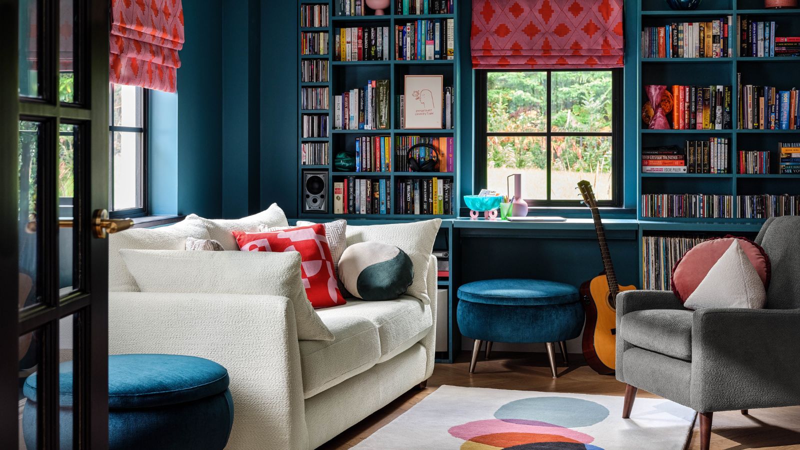 A dark blue living room with built-in bookshelves around a window. A white sofa beside them, opposite a grey arm chair. 