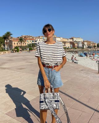 A french woman wears a striped T-shirt with denim shorts