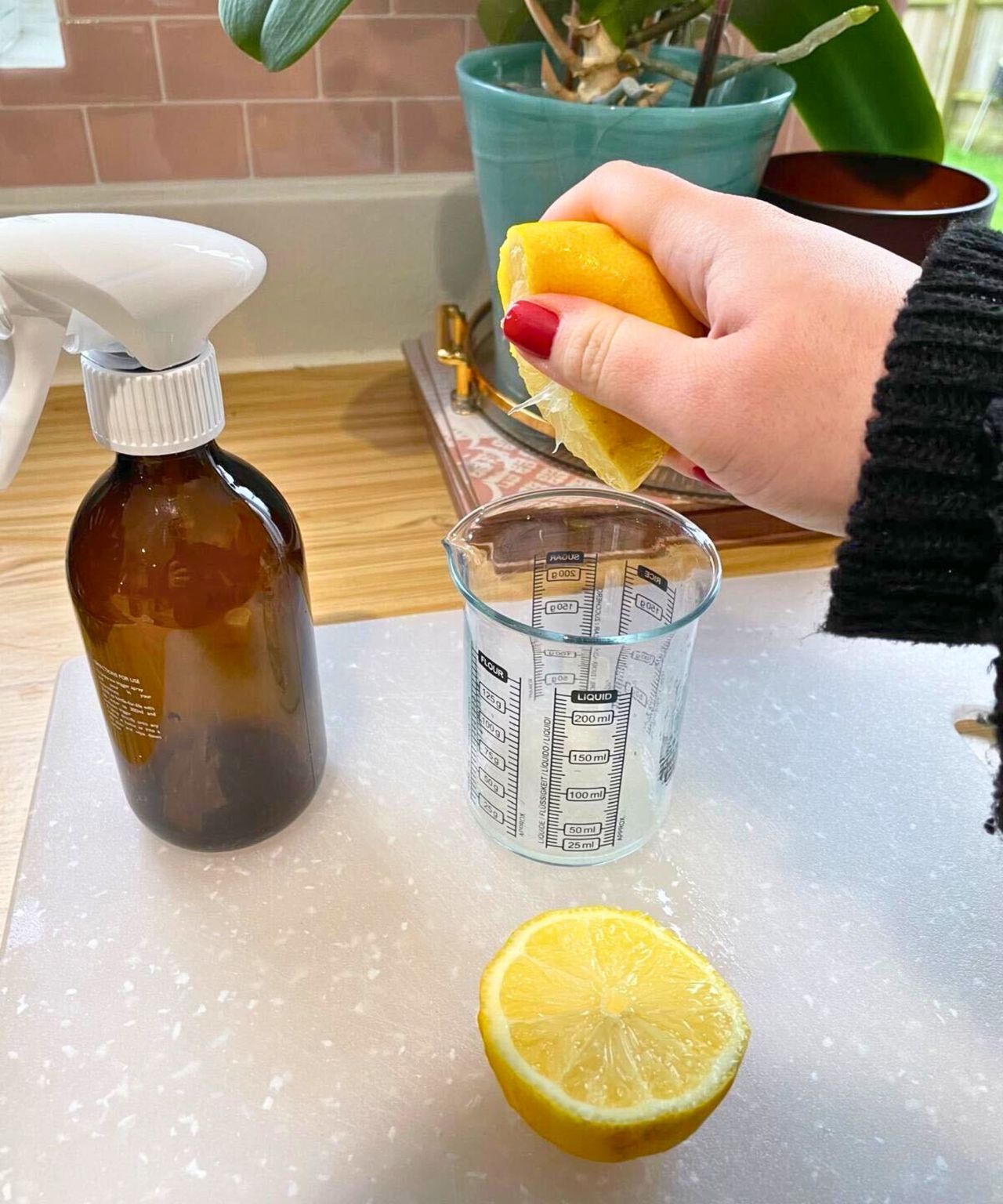 My hand squeezing half a lemon's juice into a glass small measuring cup