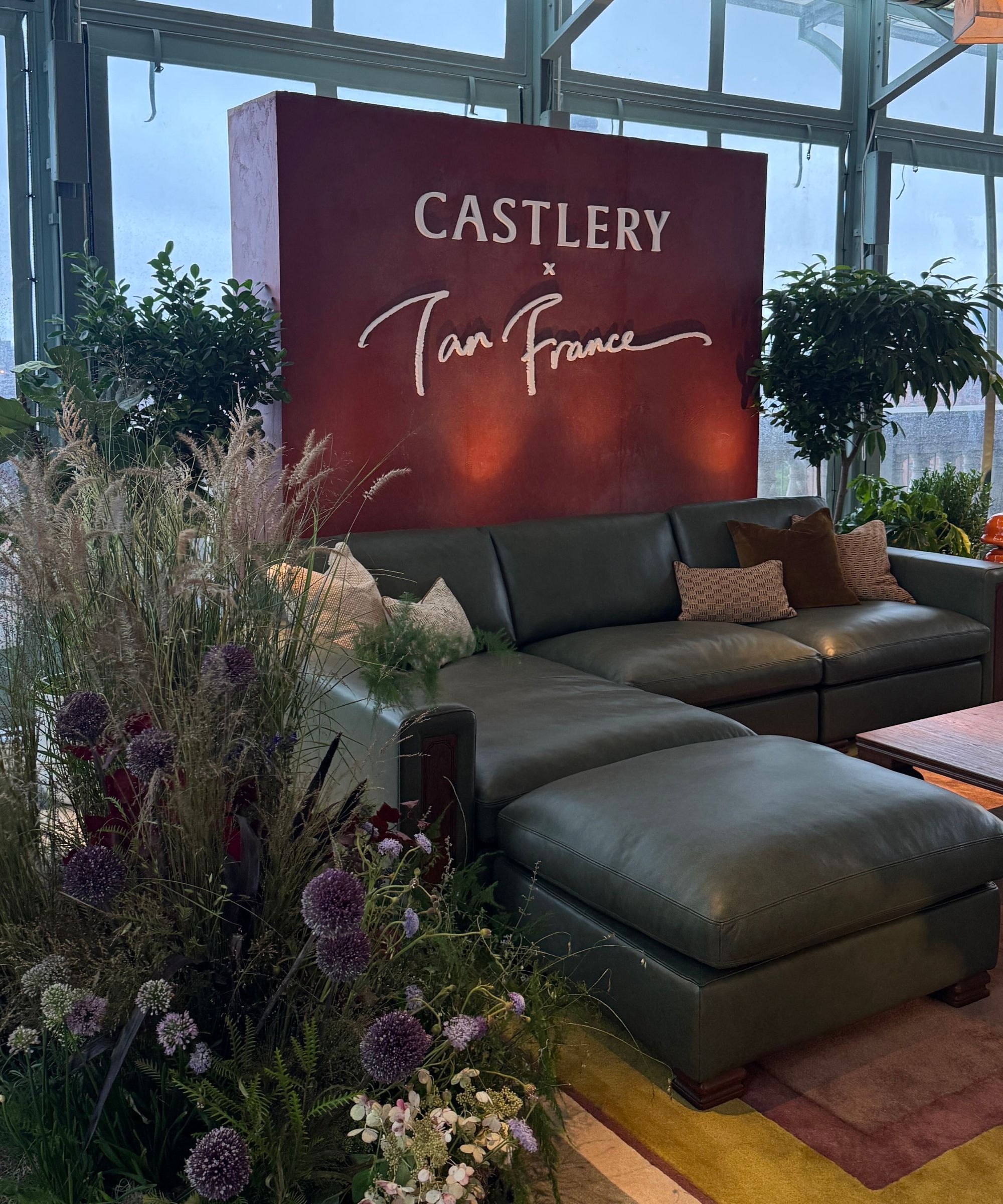 Castlery x Tan France green leather sofa in front of sign saying 'Castlery x Tan France' with large floral display