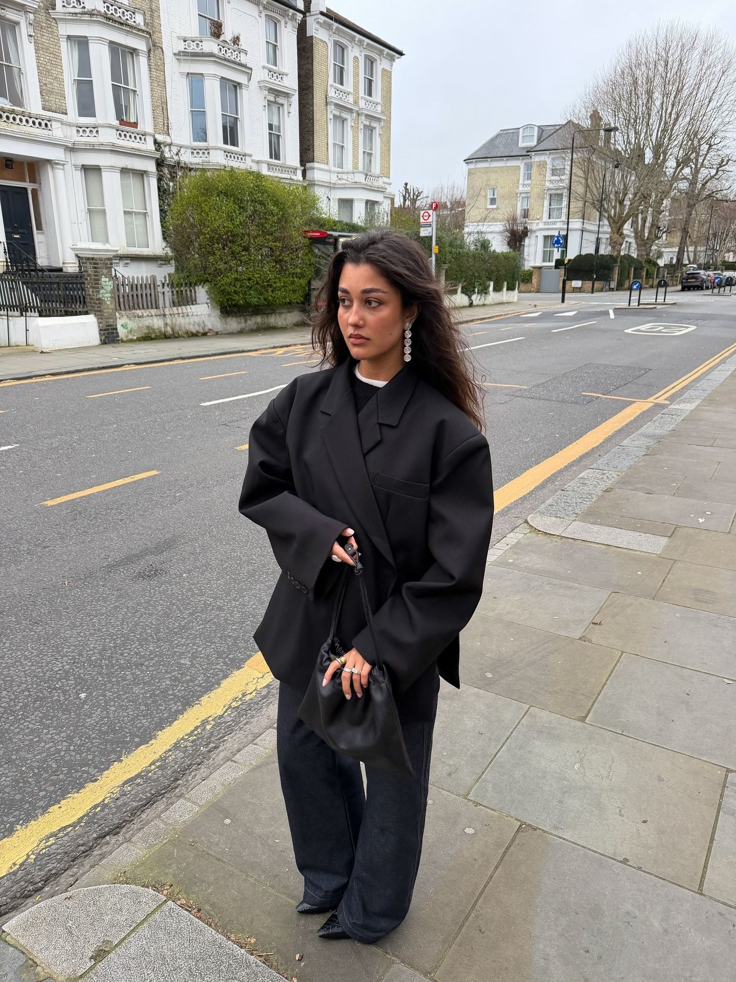 Woman wears black blazer, black jeans and carries black drawstring bag from The Horse