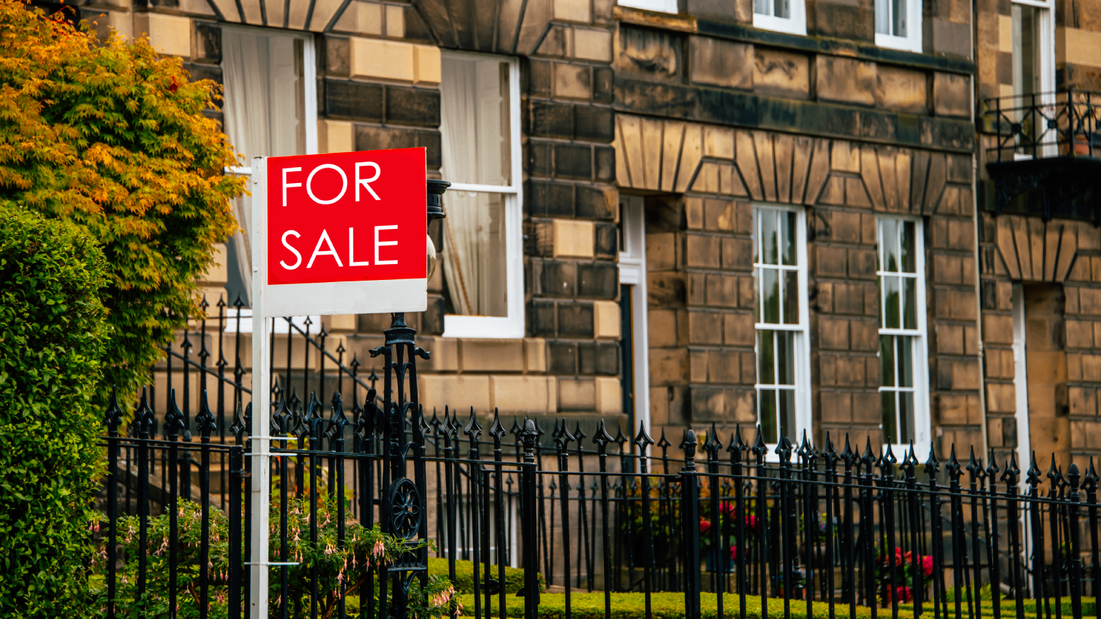 row of stone terraced town houses with for sale sign outside