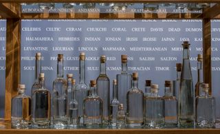 Bottles full of water of different sizes are set on a wooden shelf.