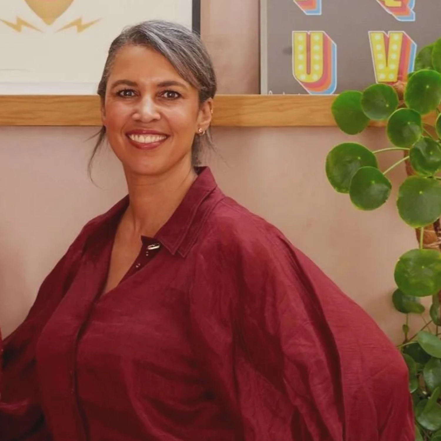 A woman with salt and pepper hair swooped back, in a maroon long sleeve blouse by a Chinese money plant
