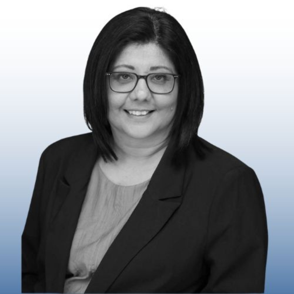 Black-and-white photo of a smiling woman with dark bob haircut and glasses, wearing a black blazer.