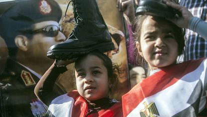 A portrait of Abdel Fattah al-Sisi behind two Egyptian girls