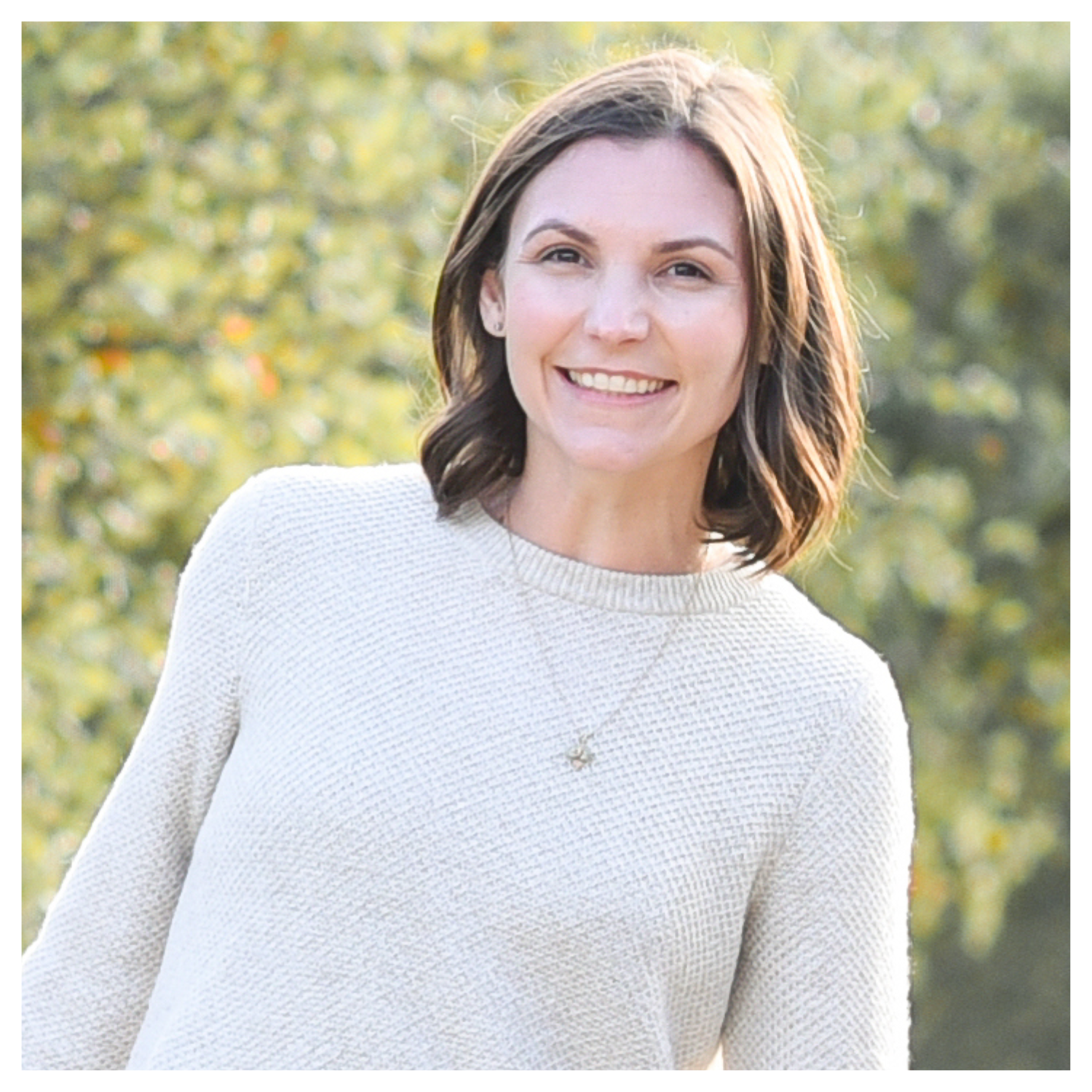 A woman with a brown long bob in a wool sweater, smiling outdoors