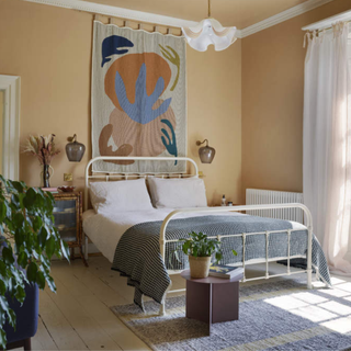 A metal bed frame sits beneath a tapestry in a neutral bedroom
