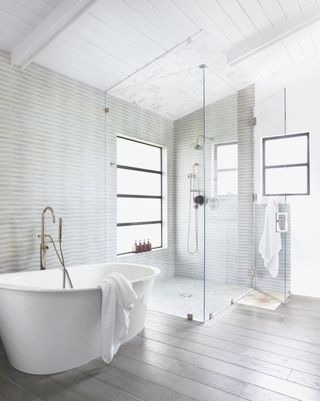 walk in shower with white tub, grey wallpaper, grey planks, glass shower wall