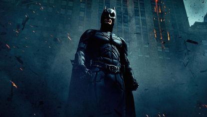 A promotional image for 2008's The Dark Knight, one of the entries in our Batman movies in order guide, which shows Batman in front of a burning building