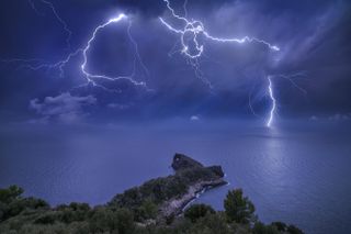 Lightning cracks the sky over Mallorca Spain. According to photographer Marc Marco Ripoll, &quot;I tried many times to catch a good lightning strike behind this rock called Sa Foradada, but every time I tried, the conditions were not so good. This night I knew that a big storm was approaching Mallorca and all the conditions were perfect. I don&#039;t remember if the moon was full, but I remember that it was very big. This was perfect, because the moon was going to illuminate all the land and the sea and gives more color to the scene. I chose my composition, and I shot many pictures until the storm fell on me. To see the storm and the lightning that night was something amazing.&quot;