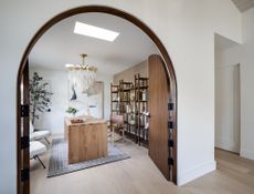 Closet office ideas: closet home office with wooden desk, wooden shelving, rug, statement pendant light, artwork, chairs 