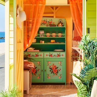 orange painted beach hut with orange curtain and green painted dresser