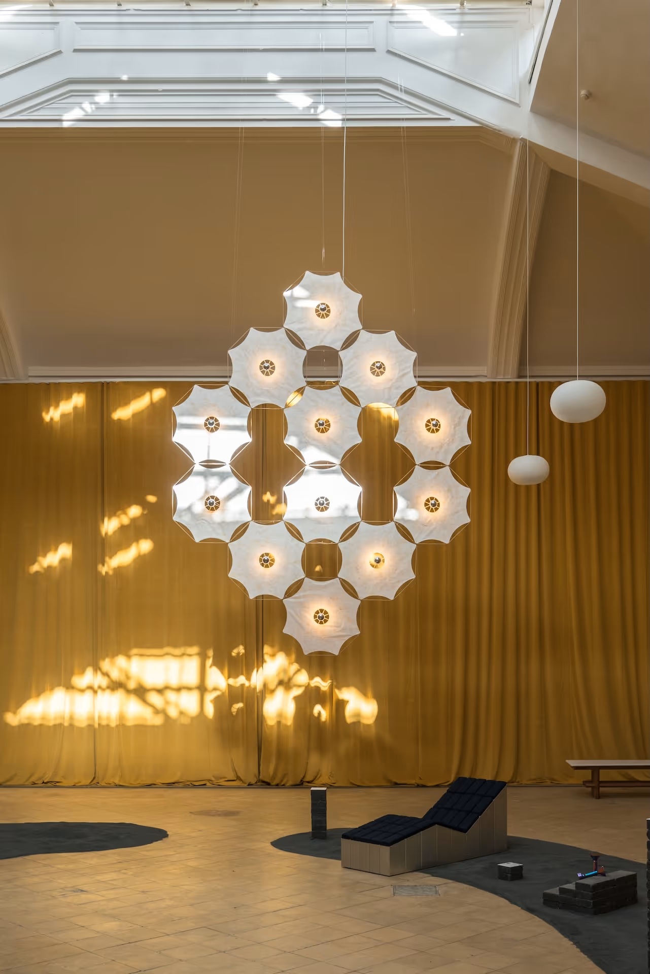 A floating lighting installation features a perforated, semi-transparent white body shaped like a leaf, with two more pendant lights showcased next to it in a naturally lit, bathing-in-sunshine room.