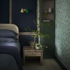 bedroom with blue and green painted walls and leafy wallpaper and blue bed