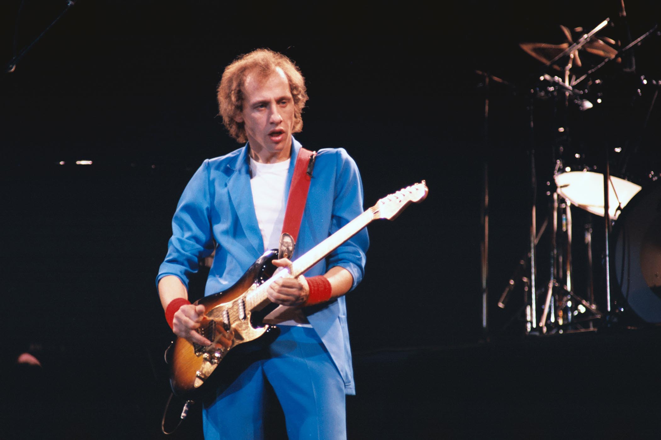 Mark Knopfler rocks Wembley with his Strat, wearing a light blue suit and white T-shirt.