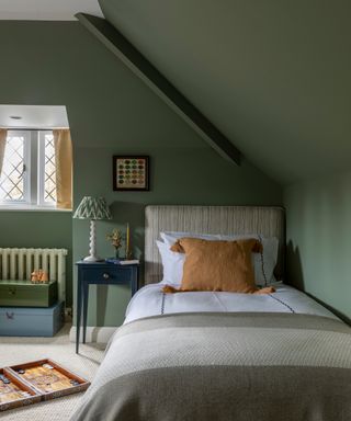 green bedroom with sloping roof and single bed, mustard cushion and dark blue bedside chest