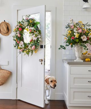 White kitchen with colorful spring wreath on door, seasonal spring foliage in vase