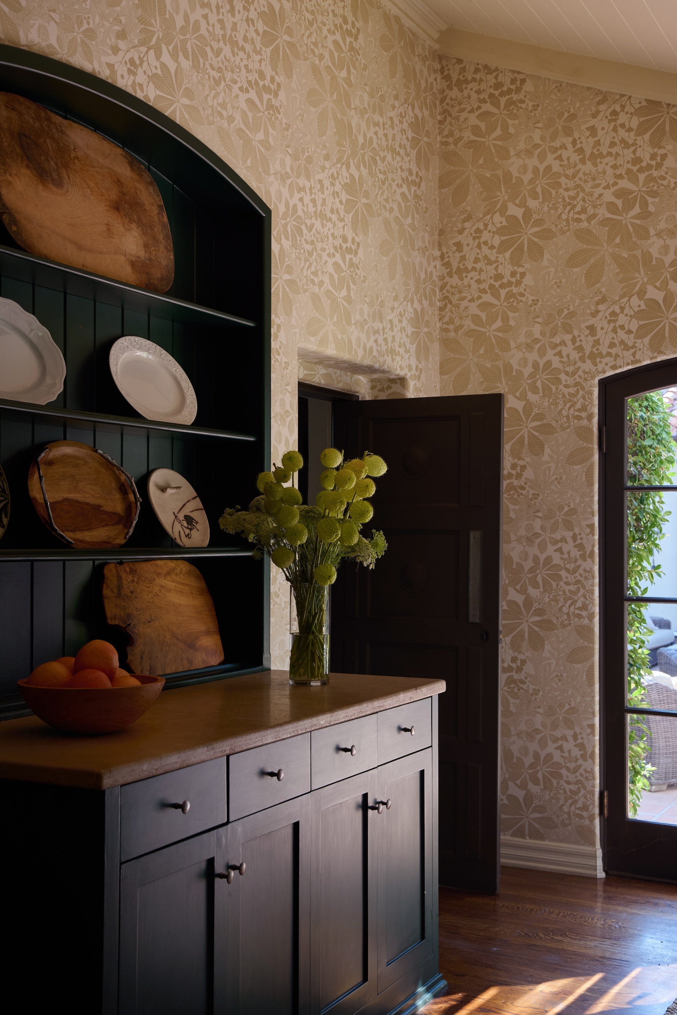 gold and white floral wallpaper with large open cabinet in dark teal color with brown wood base.