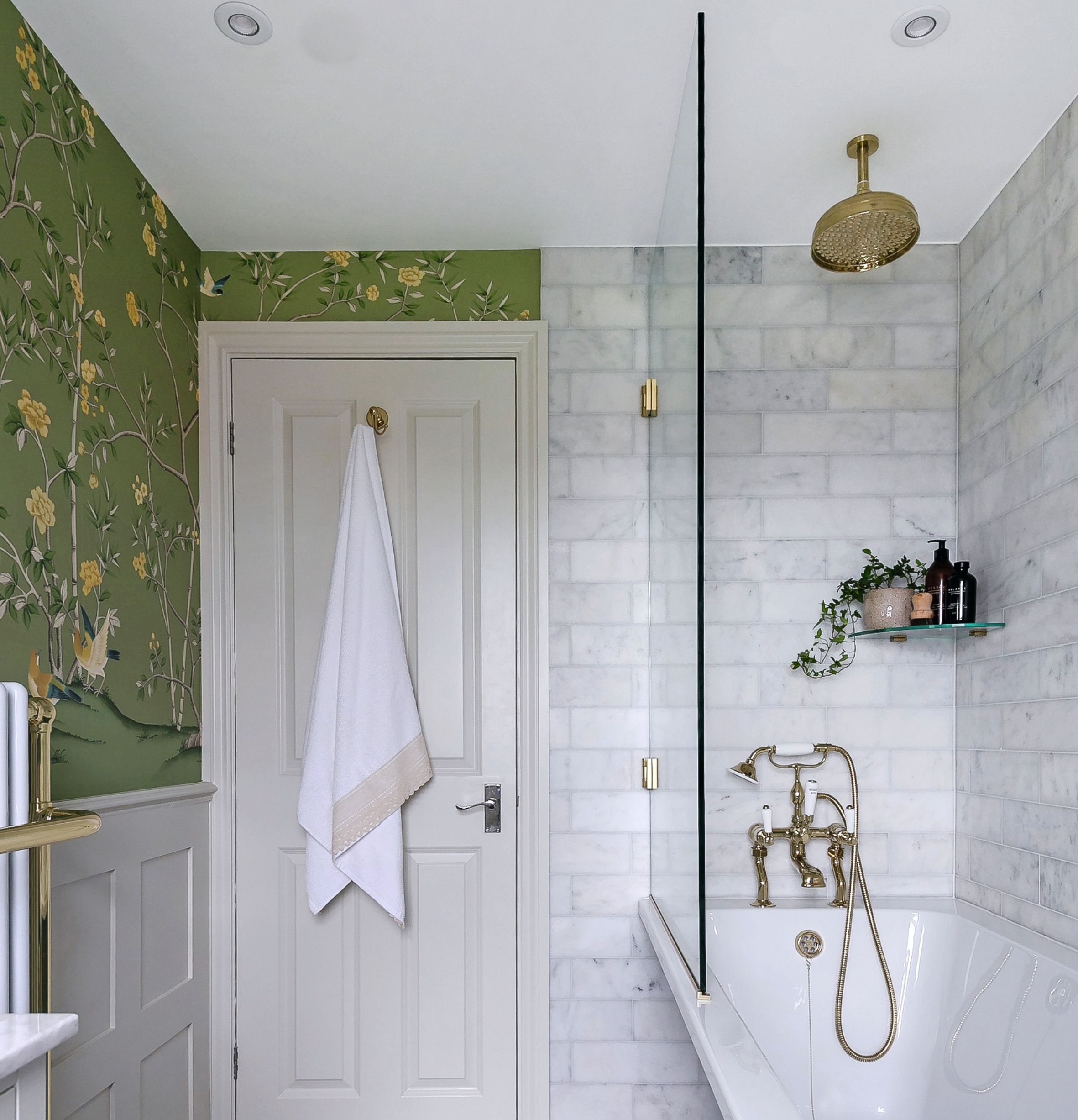 Bathroom view to door, green wallpaper, marble wall tiles, gold rainfall shower head over tub and white door