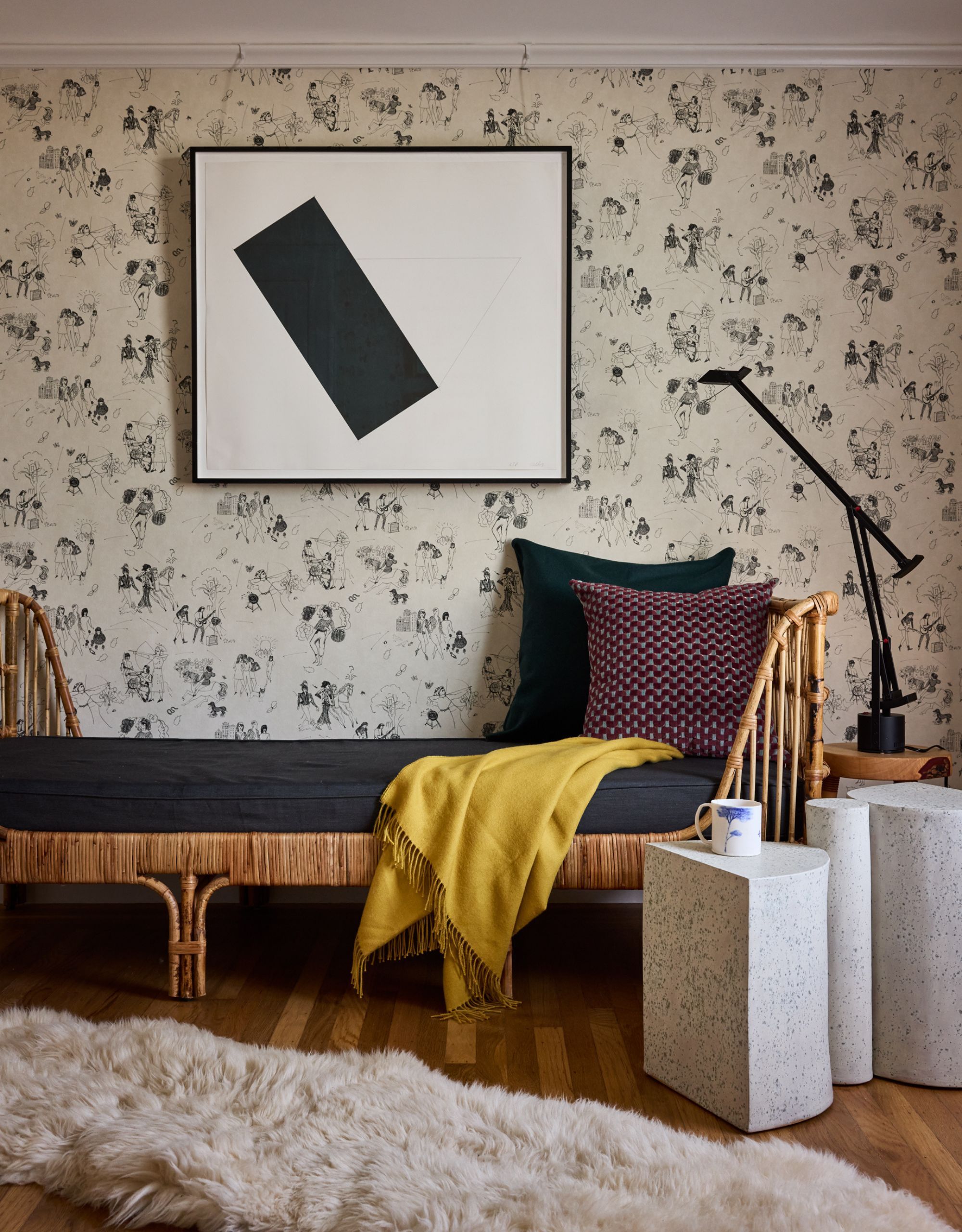 A guest bedroom with a daybed with cushions and a throw blanket on top, patterned wallpaper and wall art with an abstract side table
