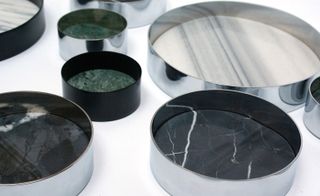 View of multiple round 'Pli' trays in silver and black, green and white marble colours against a white background