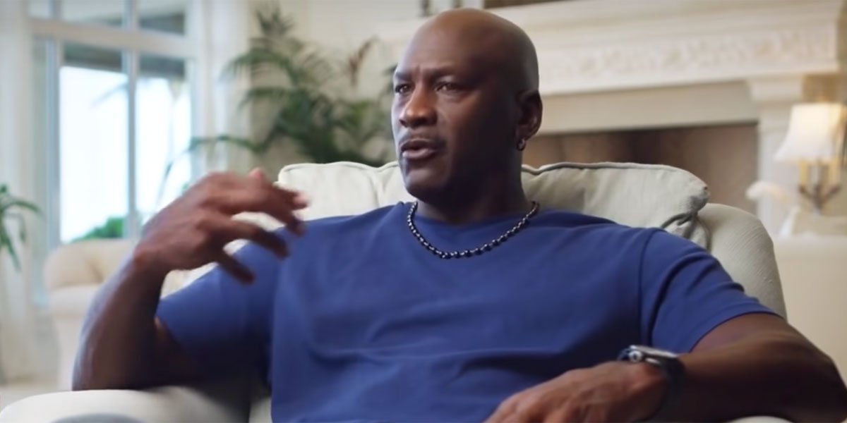 Michael Jordan being interviewed in a blue shirt sitting on a white chair.