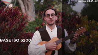 A ukulele player standing outside in front of a bush