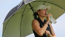 Female golfer drinking water and shading herself with an umbrella in the sun