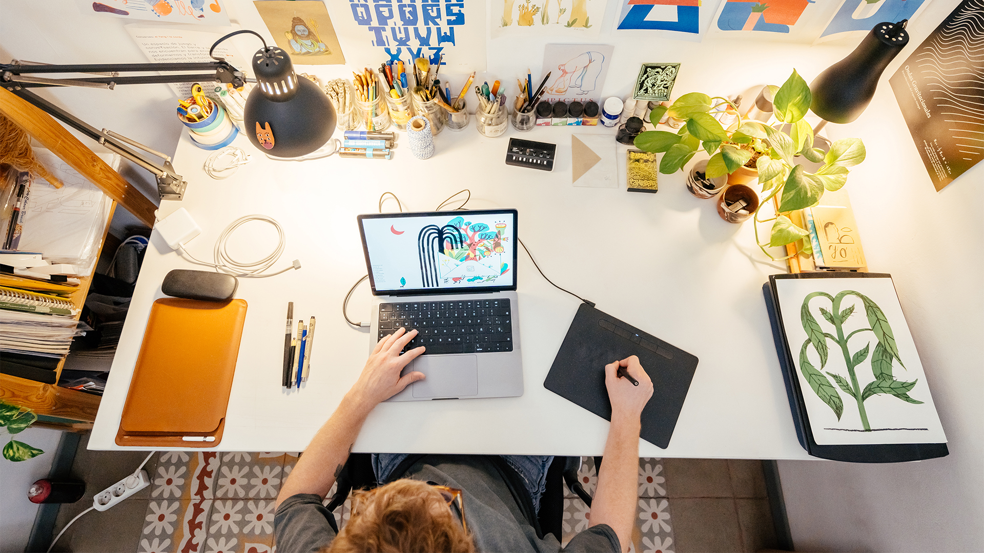 Young adult male illustrator working at the desk in a small workshop at home.