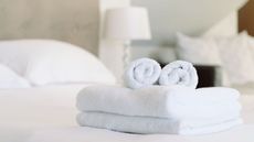 An example of the best bath towels - folded and rolled fluffy white towels on a bed in a traditional white bedroom