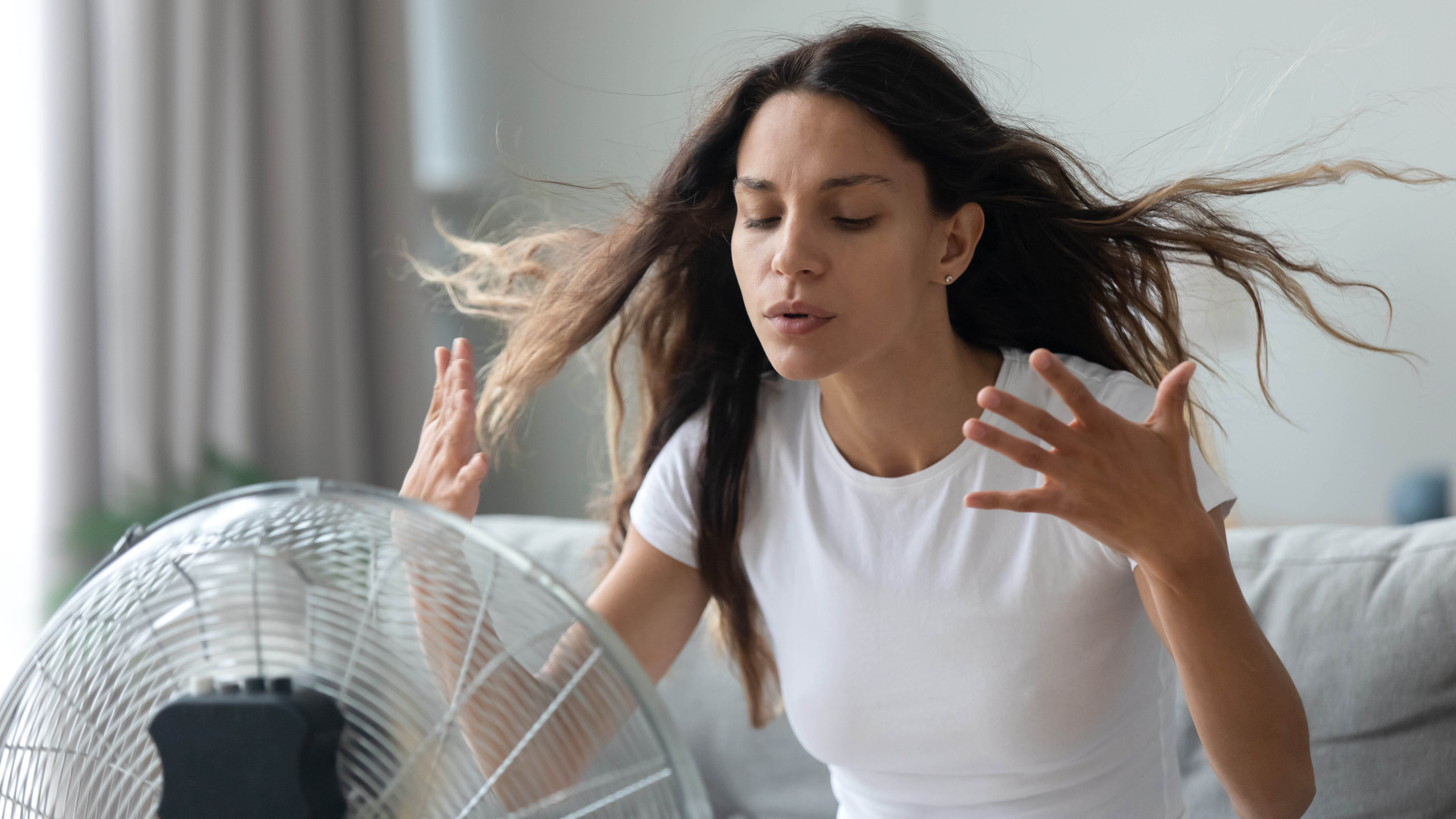 Женщина пытается сохранять прохладу перед электрическим вентилятором