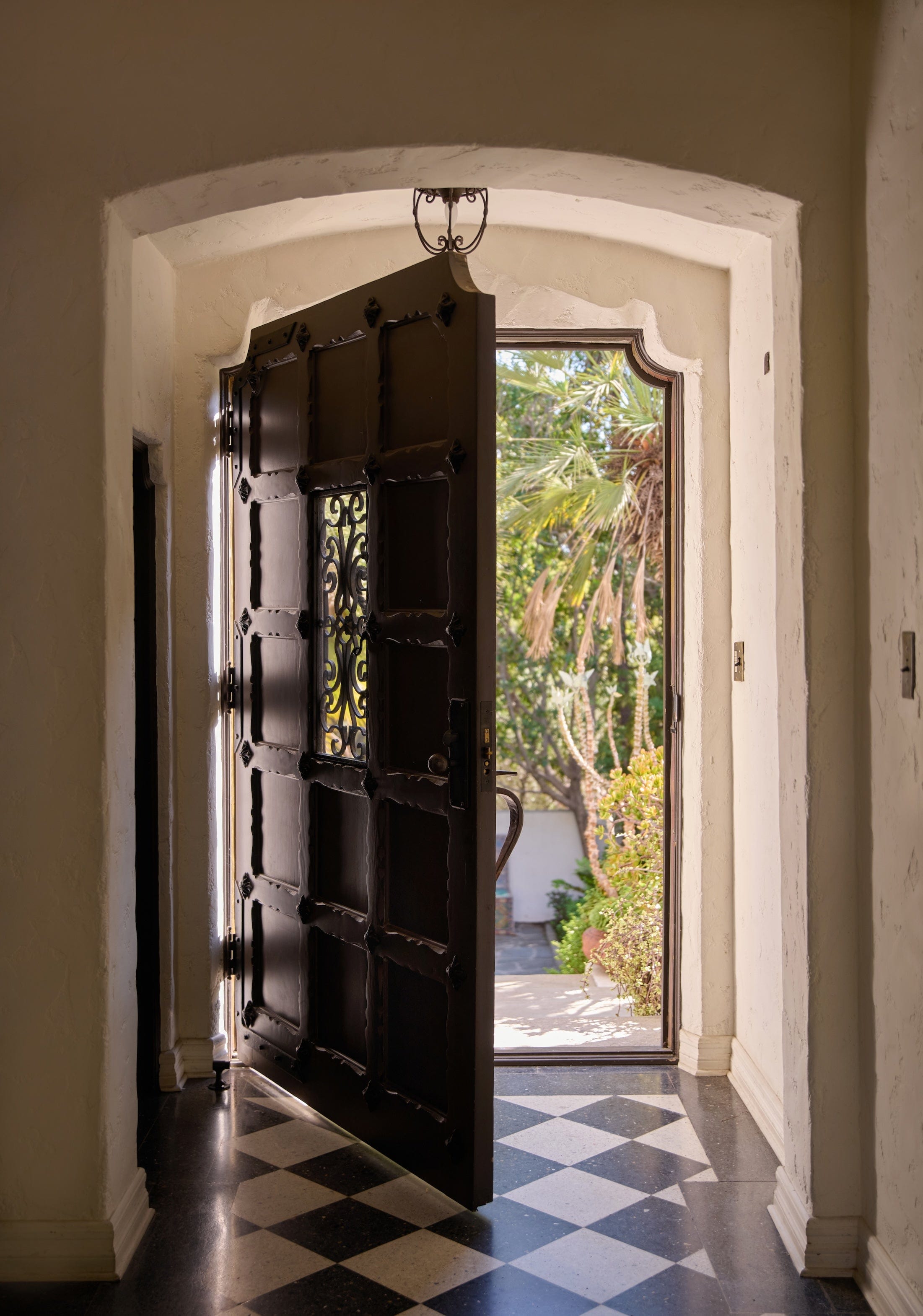 Entryway with checkerboard floor tiles and wide antique door half open. 