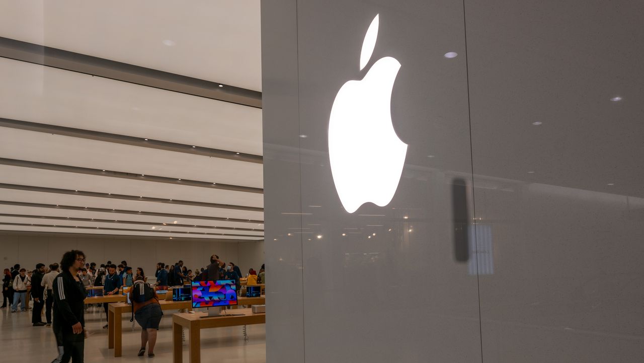 People in an Apple store with a wall showing the Apple logo.