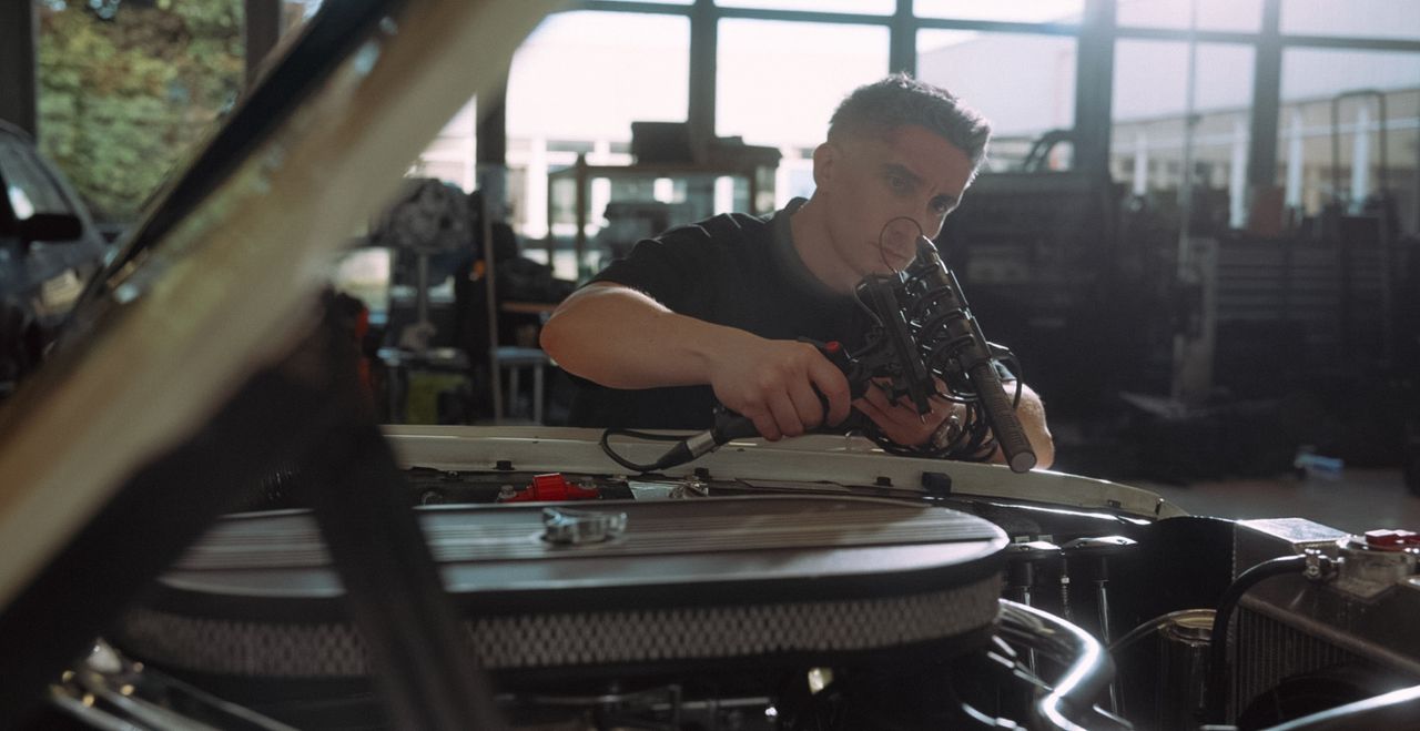 A man holding a microphone to the engine of a Mustang.