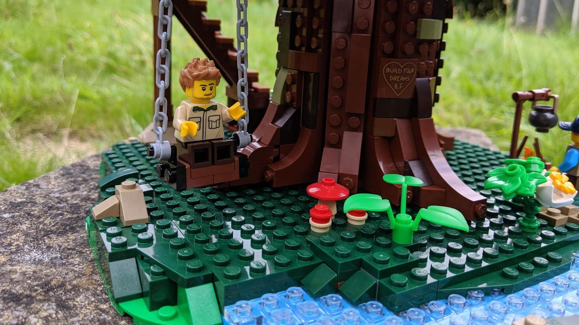 Lego Ideas Tree House 21318 - close up of base of tree house (man on swing, river, plants).