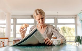 Woman eating a pastry and drinking coffee while reading the paper