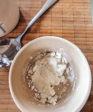 A birds eye view of a ceramic pot with baking soda in it, on a wooden chopping board with a metal spoon