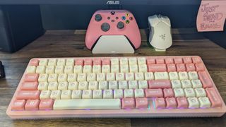 A wood desk with a pink keyboard, gamepad, and a white Razer Viper Ultimate mouse on a charging dock