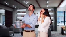 Distressed couple holding a bucket to catch a water leak in their roof
