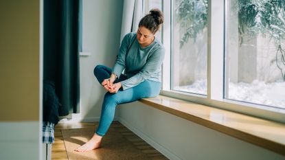Woman sits on window seat rubbing her foot